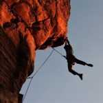 Rock climber using rope clamps for secure ascending on natural stone wall during outdoor climbing