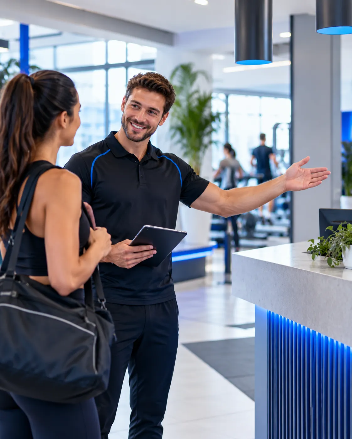 Vriendelijke fitnessmedewerker verwelkomt een vrouwelijke bezoeker en geeft uitleg bij de receptie van een moderne fitnessruimte.